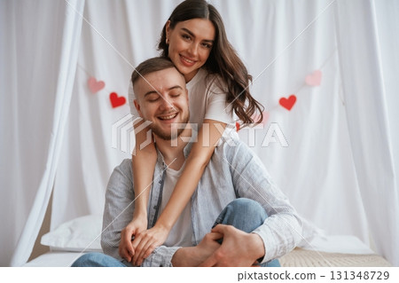 Happy facial expressions, red heart shaped decoration behind. Young couple are together at home Happy facial expressions, red heart shaped decoration behind. Young couple are together at home 131348729