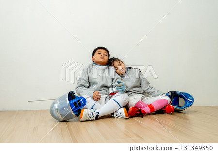 Front view of Asian brother and sister with fencing sport uniform sit beside and look tired also relax after practice for competition. 131349350