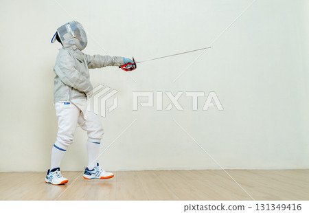 Asian boy with fencing sport uniform stand and point epee to his front direction to act of practice for the competion. Asian boy with fencing sport uniform stand and point epee to his front direction to act of practice for the competion. 131349416