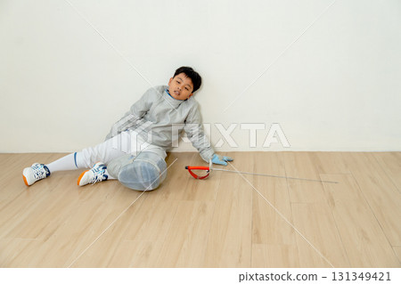 Asian boy with fencing sport uniform sit on the floor and look tired also relax after practice for competition. 131349421