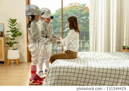 Asian mother sit on bed and take care uniform and tools of her child for fencing sport practicing at home. Asian mother sit on bed and take care uniform and tools of her child for fencing sport practicing at home. 131349429