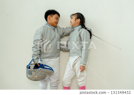 Asian brother and sister with fencing sport uniform hug together also look at face and smile to relax during practice for competition. Asian brother and sister with fencing sport uniform hug together also look at face and smile to relax during practice for competition. 131349432