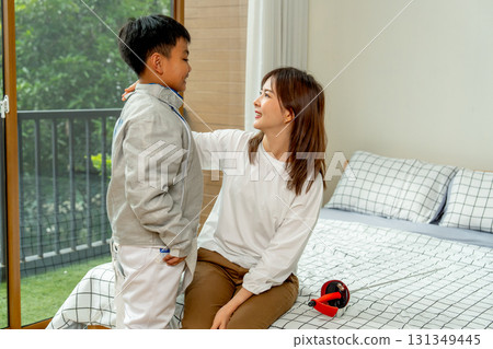 Close up Asian mother sit on bed and touch shoulder of her son to encourage during practice fencing sport in bedroom with soft morning light and happiness. 131349445