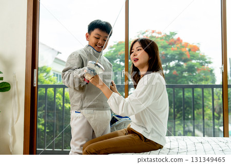 Asian mother sit on bed and encourage her son to practice fencing sport at home. 131349465