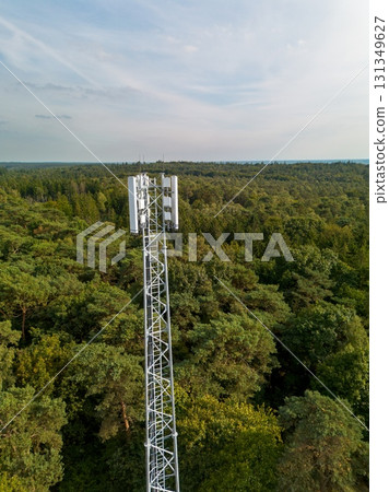 Aerial view of dense forest with a tall telecom tower and dirt access road highlighting the intersection of technology and natural landscape. Aerial view of dense forest with a tall telecom tower and dirt access road highlighting the intersection of technology and natural landscape. 131349627
