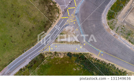 Aerial view of curved and straight roads with traffic markings, arrows, and signs, set in grassy terrain possibly a test track or training site. 131349636
