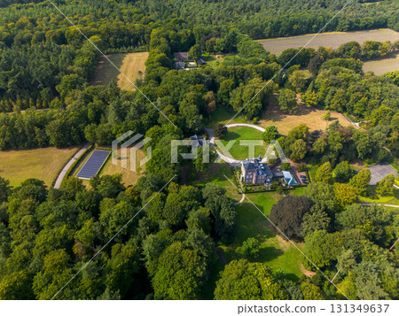 Aerial view of forested estate with central mansion, circular driveway, adjacent buildings, solar panels, and surrounding fields blending tradition, nature, and sustainability. 131349637