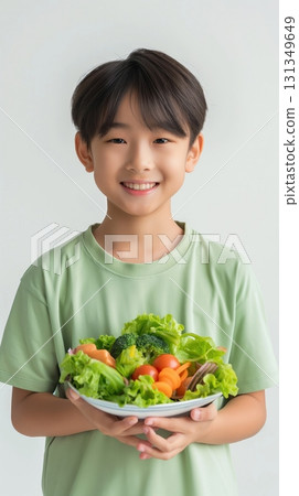 A young boy is holding a bowl of vegetables, including broccoli and carrots A young boy is holding a bowl of vegetables, including broccoli and carrots 131349649