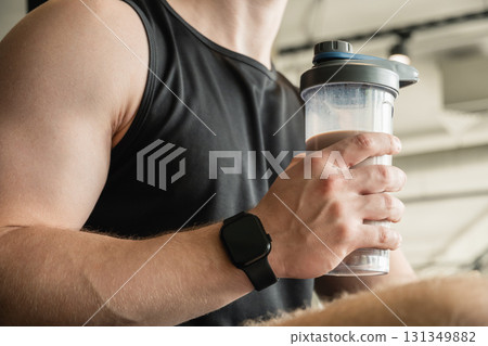 Young bodybuilder and sporty man with protein shake while working out at gym or fitness center. Health care and workout. 131349882