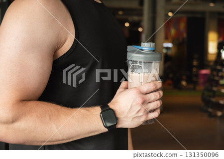 Protein shaker in man hand at gym or fitness center. Health care and workout. Close up. 131350096