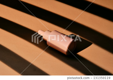 A bottle of serum on a beige background with stripes of shadows. A bottle of serum on a beige background with stripes of shadows. 131350119