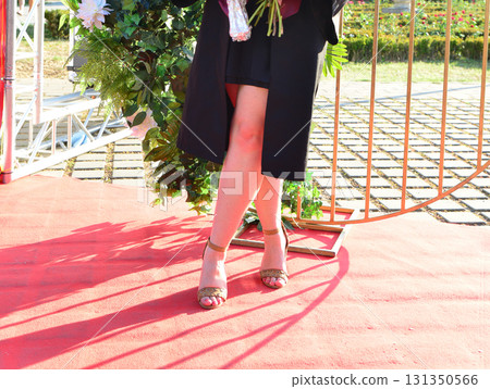 Elegant female student poses proudly in graduation outfit showing beautiful legs and high heels Elegant female student poses proudly in graduation outfit showing beautiful legs and high heels 131350566