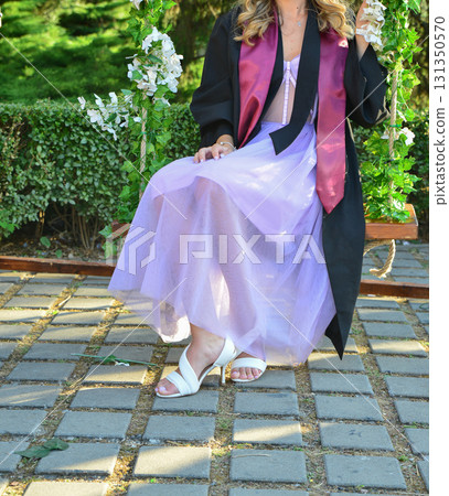 Elegant female student poses proudly in graduation outfit showing beautiful legs and high heels 131350570