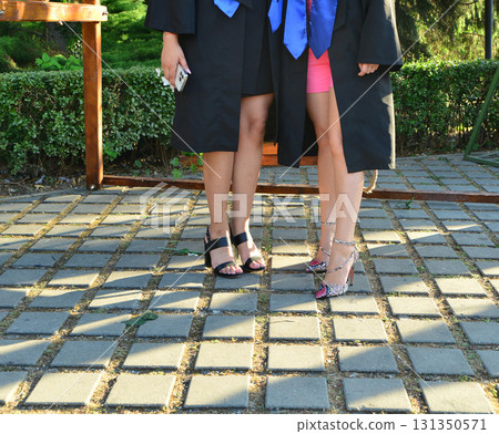 Elegant female student poses proudly in graduation outfit showing beautiful legs and high heels 131350571