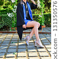 Elegant female student poses proudly in graduation outfit showing beautiful legs and high heels 131350576