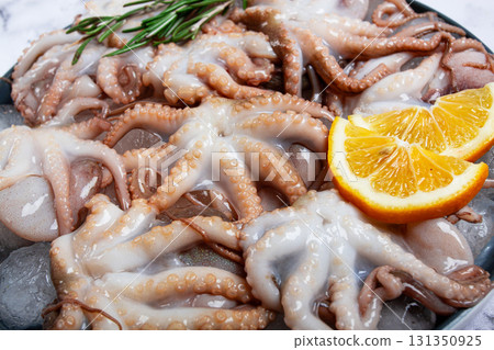 Fresh baby octopuses on ice, garnished with lemon and rosemary, on a marble table, no people, 131350925