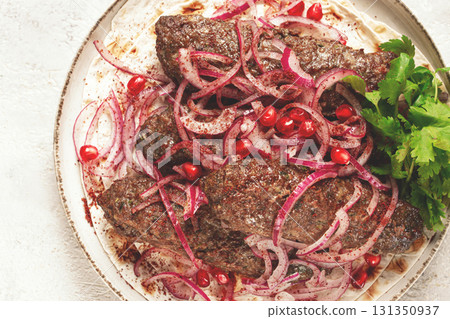 grilled kebabs topped with onions and pomegranate on a white plate in a bright kitchen setting grilled kebabs topped with onions and pomegranate on a white plate in a bright kitchen setting 131350937