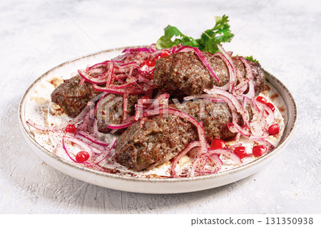 grilled kebabs topped with onions and pomegranate on a white plate in a bright kitchen setting grilled kebabs topped with onions and pomegranate on a white plate in a bright kitchen setting 131350938