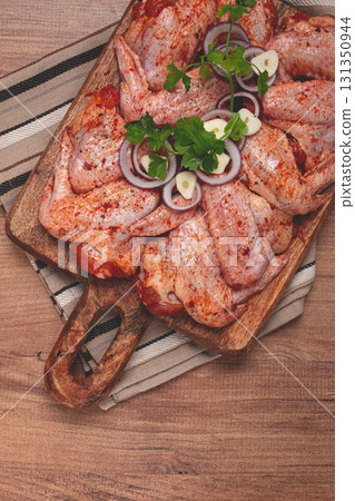 Chicken wings, marinated and laid out on a wooden platter, ready for cooking, grilling or baking, in a home kitchen, there are no people 131350944