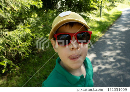 Portrait of an eight-year-old boy wearing glasses and cap showing his tongue or licking his lips. Portrait of an eight-year-old boy wearing glasses and cap showing his tongue or licking his lips. 131351009