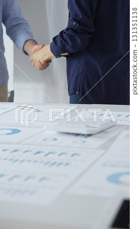 Professional businesspeople concluding deal, shaking hands near financial paperwork, calculator, pen on pristine workspace surface. Handshake concept 131351138