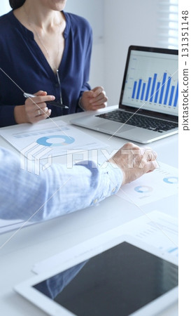 Businessman and businesswoman are analyzing financial data on a laptop and looking through documents, pointing at charts and graphs during a meeting in bright office. Business people concept 131351148