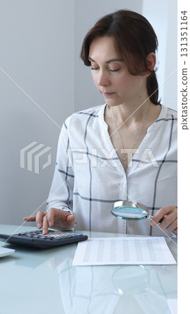 Accountant carefully reviewing financial documents, magnifying details, calculating performance metrics at professional workspace. Audit and taxes in business Accountant carefully reviewing financial documents, magnifying details, calculating performance metrics at professional workspace. Audit and taxes in business 131351164