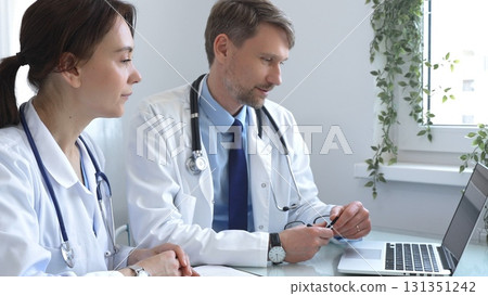 Two doctors are carefully studying medical charts on a laptop, discussing patient medical histories in a hospital or clinic. Medicine and healthcare concept. Two doctors are carefully studying medical charts on a laptop, discussing patient medical histories in a hospital or clinic. Medicine and healthcare concept. 131351242
