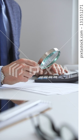 Professional businesswoman carefully reviewing financial reports using magnifying glass and calculator, conducting thorough analysis of business performance. Audit and taxes in business Professional businesswoman carefully reviewing financial reports using magnifying glass and calculator, conducting thorough analysis of business performance. Audit and taxes in business 131351271