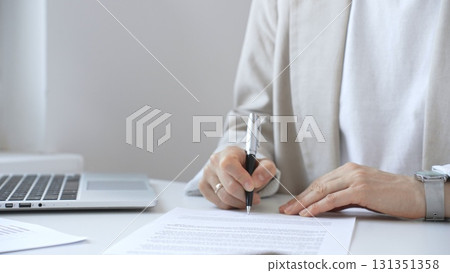 Businesswoman signing a contract at her office desk, surrounded by a laptop and documents, exemplifies focus and commitment. Business people concept 131351358