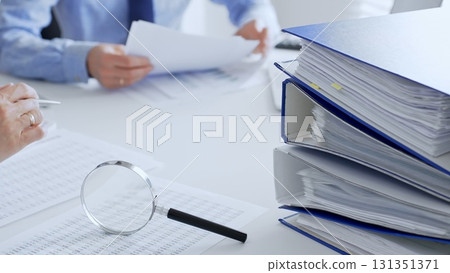 Accountants are analyzing financial reports with magnifying glass and documents, performing accounting and auditing tasks in the office, close up. Audit and taxes in business 131351371