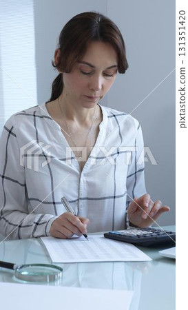 Female professional calculating finances, reviewing paperwork, tracking business expenses with precision and focus. Audit and taxes in business Female professional calculating finances, reviewing paperwork, tracking business expenses with precision and focus. Audit and taxes in business 131351420