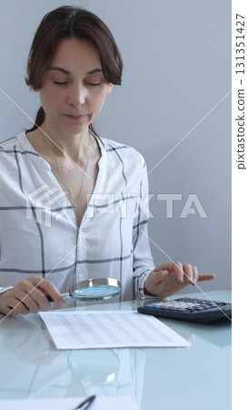 Accountant carefully reviewing financial documents, magnifying details, calculating performance metrics at professional workspace. Audit and taxes in business Accountant carefully reviewing financial documents, magnifying details, calculating performance metrics at professional workspace. Audit and taxes in business 131351427