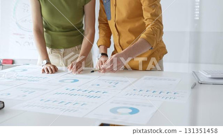 Business professionals analyzing financial reports, pointing at data points on charts and graphs lying across white desk surface 131351458