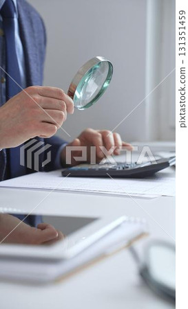 Financial professional analyzing company reports with magnifying glass, checking detailed metrics and verifying accounting precision on desk workspace. Audit and taxes in business 131351459