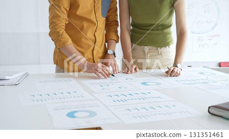Professional team analyzing financial charts, collaborating intently around conference table in sleek, contemporary workspace. Business people concept 131351461
