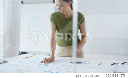 Businesswoman pointing at financial charts and graphs on a table, with a pie chart on a flip chart in the background. Business people concept 131351475