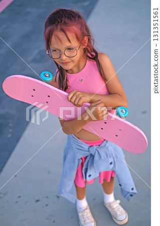 A stylish girl stands with a skateboard in hands in a skate park. Skate riding skills. Active sports hobbies A stylish girl stands with a skateboard in hands in a skate park. Skate riding skills. Active sports hobbies 131351561
