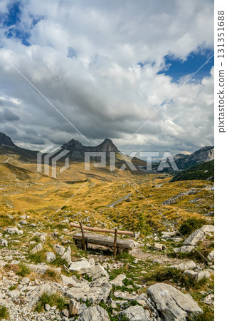 Wooden bench overlooking a saddle-shaped mountain partially covered by clouds in Sedlo, Montenegro, with scenic park surroundings 131351688