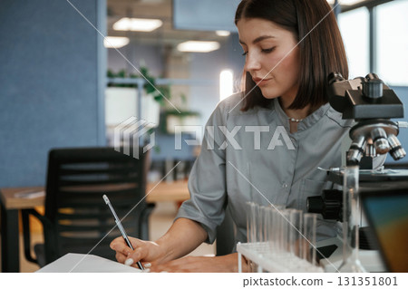 By the microscope. Female doctor in coat is indoors By the microscope. Female doctor in coat is indoors 131351801