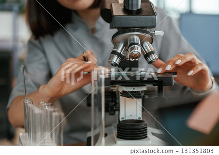By the microscope. Female doctor in coat is indoors 131351803
