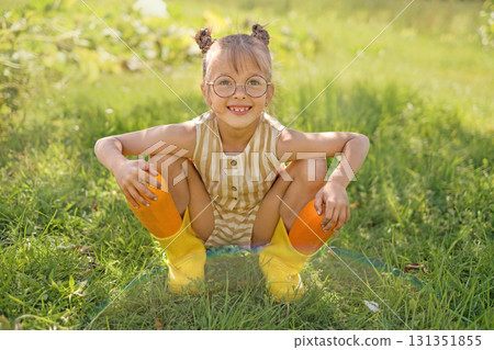 A funny smiling girl with glasses hides large zucchini in rubber boots. Healthy eco-organic vegetables A funny smiling girl with glasses hides large zucchini in rubber boots. Healthy eco-organic vegetables 131351855