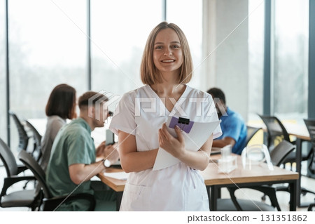 Positive woman is standing and smiling. Group of doctors are together indoors 131351862