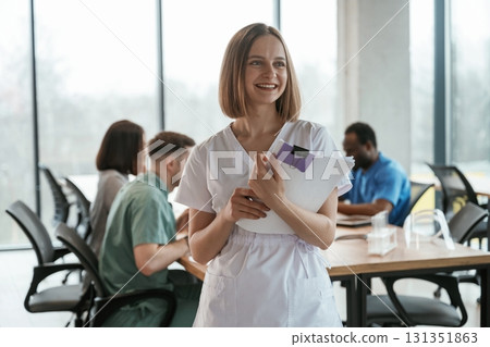 Positive woman is standing and smiling. Group of doctors are together indoors Positive woman is standing and smiling. Group of doctors are together indoors 131351863