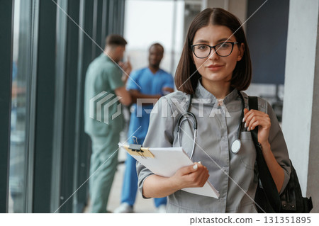 Beautiful woman in glasses is standing. Group of doctors are together indoors Beautiful woman in glasses is standing. Group of doctors are together indoors 131351895