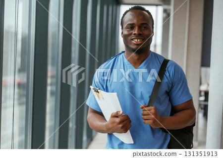 Black man doctor is standing indoors and holding documents in hands Black man doctor is standing indoors and holding documents in hands 131351913
