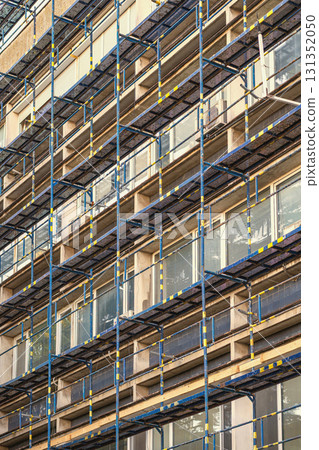 Scaffolding structure on building facade during renovation with geometric metal patterns. Concept of construction process, urban maintenance, city renovation Scaffolding structure on building facade during renovation with geometric metal patterns. Concept of construction process, urban maintenance, city renovation 131352050
