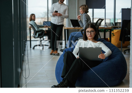 Smart woman is sitting and uses laptop. People are working in the office with bean bags chairs in it 131352239