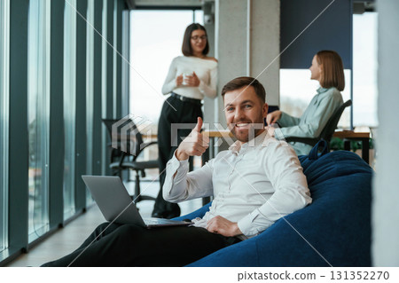 Handsome man is sitting with laptop. People are working in the office with bean bags chairs in it Handsome man is sitting with laptop. People are working in the office with bean bags chairs in it 131352270