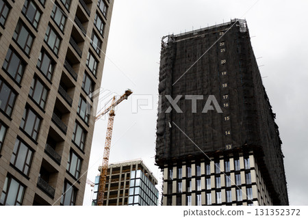View of modern construction site with partially built high rise building, showing ongoing development process. Scaffolding and crane emphasize construction work in urban architecture View of modern construction site with partially built high rise building, showing ongoing development process. Scaffolding and crane emphasize construction work in urban architecture 131352372